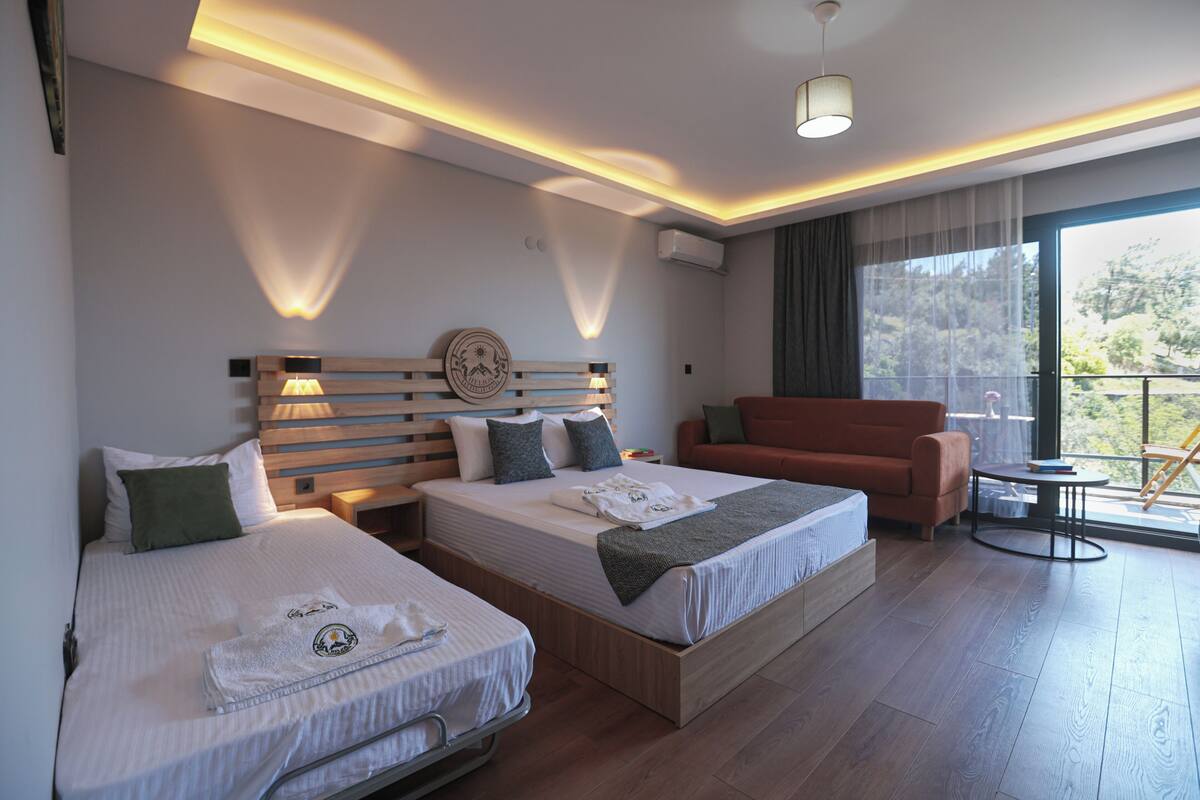 Habitación de hotel con dos camas, un sofá, un balcón con vistas y una lámpara en el techo.