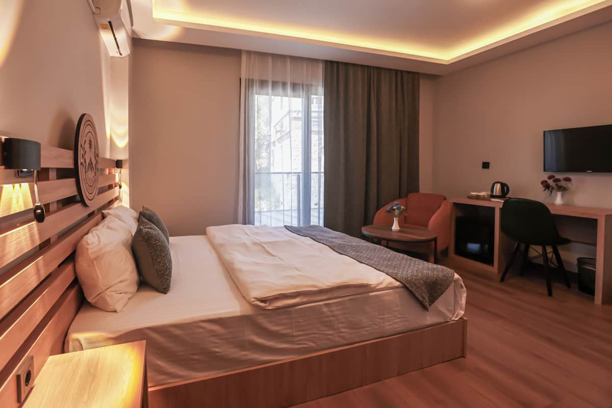 Habitación de hotel con cama, escritorio, silla, televisión y ventana con cortinas.