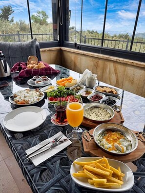 A dining table with various dishes, a glass of orange juice, and a view of the outdoors. - Helios Kaz Dağları 2.BLOK (Edremit)