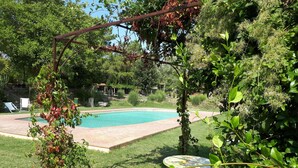 A backyard with a swimming pool, a pergola, and a table.