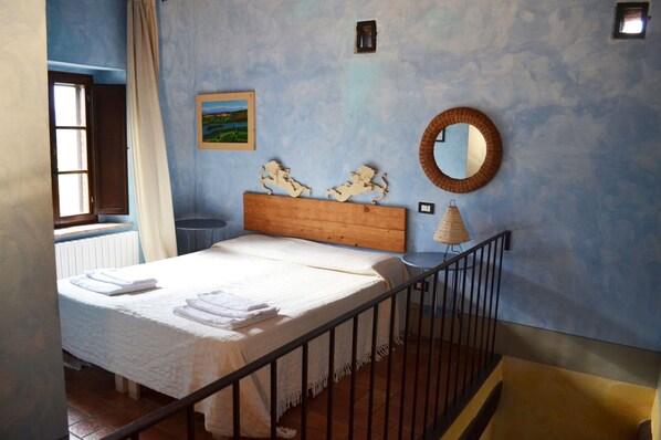 Un dormitorio con una cama de madera, un espejo redondo, una mesita y un cuadro en la pared.