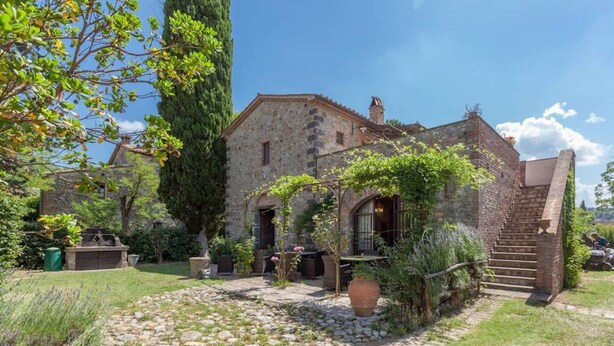 A stone house with a garden, a stone staircase, and a pergola.