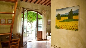 Una habitació amb sostre de fusta, taula de menjador amb cadires, finestra gran amb cortines i un quadre d'un camp a la paret.