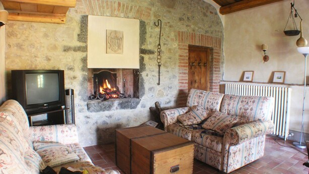 Una sala de estar acogedora con chimenea de piedra, televisor, sofás estampados y un cofre de madera.