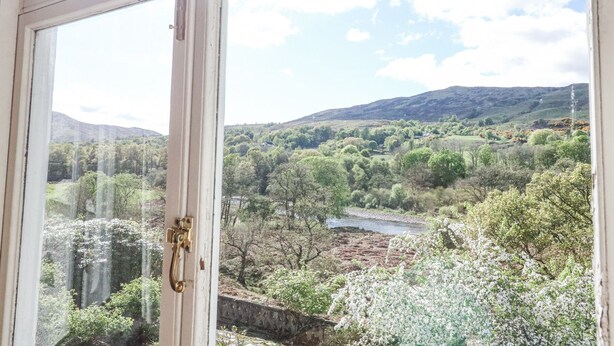 A view through a window with a brass handle, overlooking a landscape with trees, a river, and hills. - Camisky Lodge (Fort William)