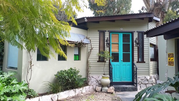 Una casa con una puerta turquesa, un pequeño porche y un muro de piedra.