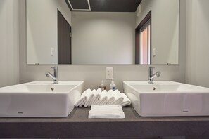 Un baño con dos lavamanos blancos, un espejo grande y toallas dobladas ordenadamente en el mostrador.
