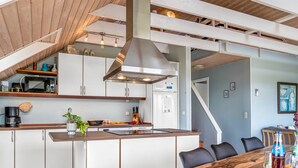 Eine moderne Küche mit weißen Schränken, einer Holzinsel und einem Essbereich mit einem großen Holztisch und schwarzen Stühlen.