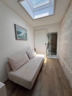 Una habitación con tragaluz, un sofá, un cuadro y una pared de piedra.