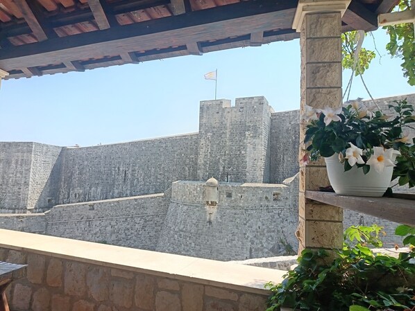 A view of a stone fortress with a flag on top, a potted plant with white flowers, and a stone wall. - Brand new apartment by City Walls Dubrovnik - perfect for 2! (Dubrovnik)