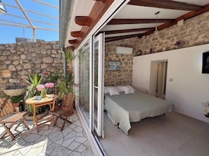 Un dormitorio con cama, una mesita con sillas, una ventana y una pared de piedra.
