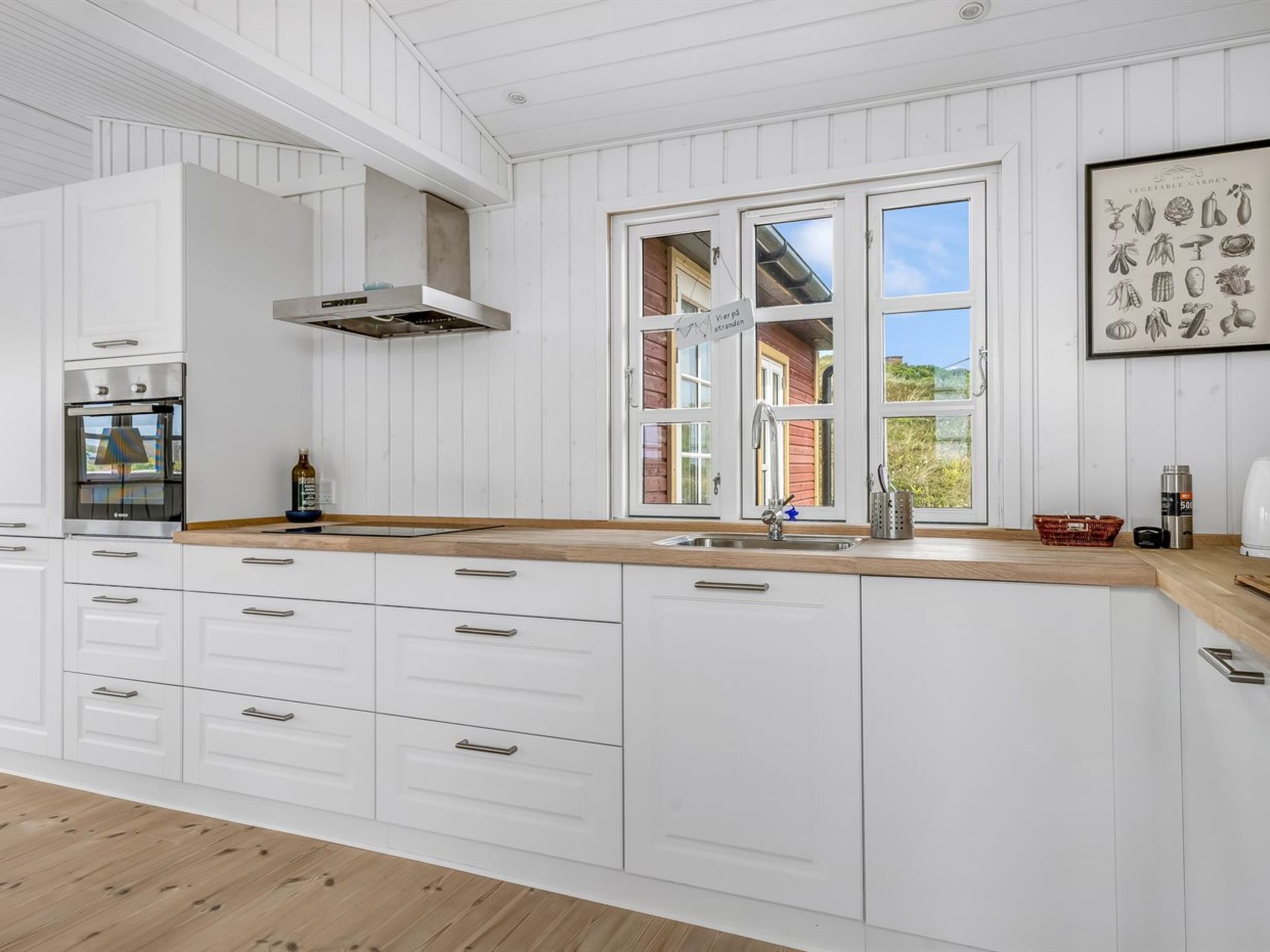 Una cocina moderna con armarios blancos, encimera de madera, horno empotrado y un amplio ventanal con vistas al exterior.