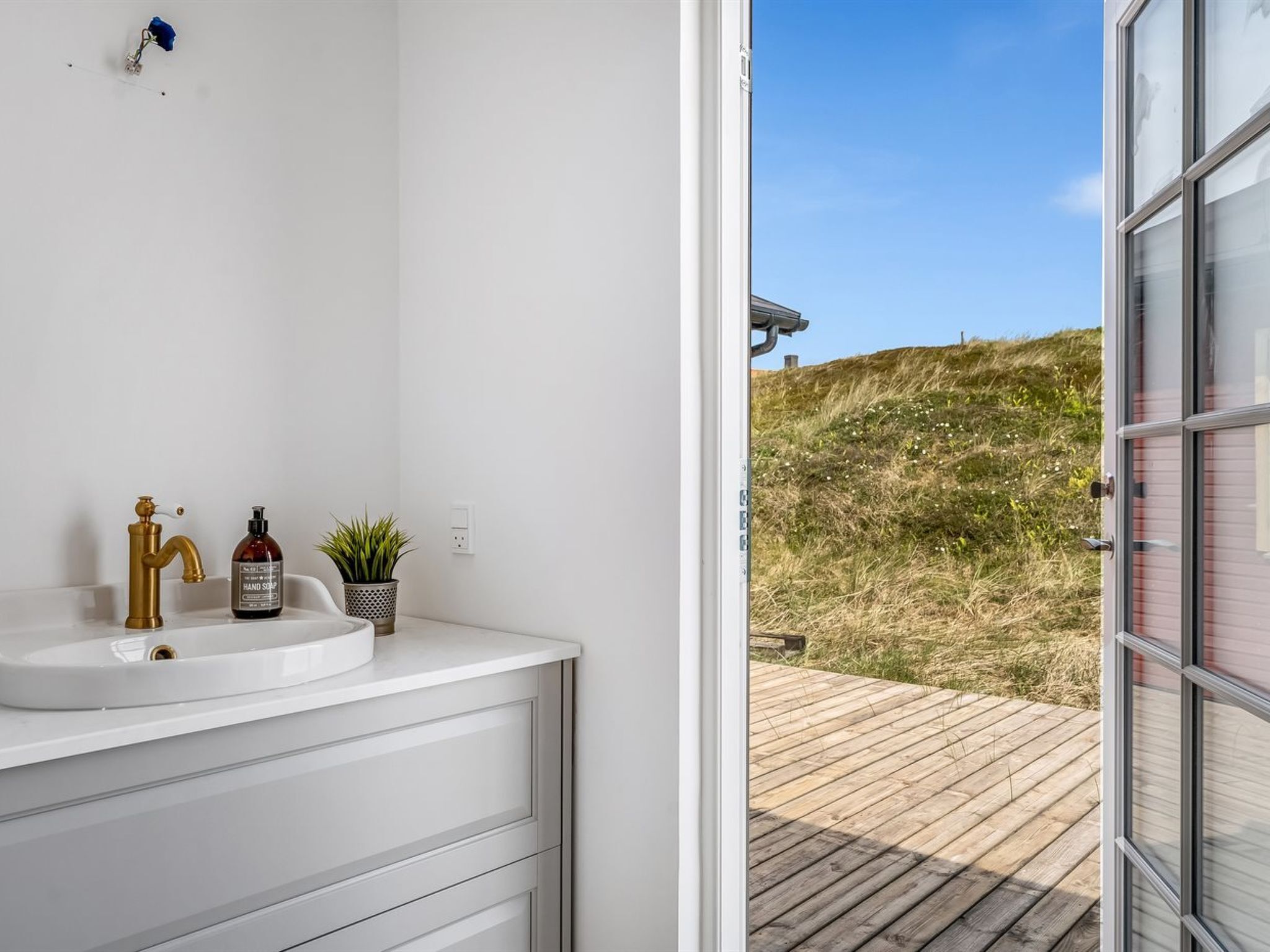 Un baño con lavamanos blanco, grifo dorado y una botella de jabón para manos.