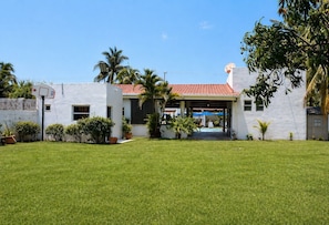 A white building with a red-tiled roof, a basketball court, and a pool.