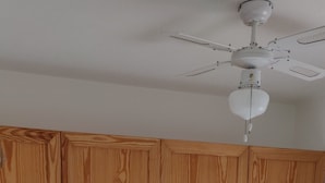 A bedroom with a wooden bed, two bedside tables, a ceiling fan, and a shelf with lamps.