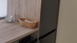 A kitchen with a wooden cabinet, a stainless steel refrigerator, a microwave, and a trash bin.