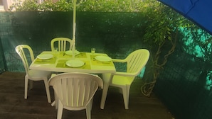 An outdoor dining area with a table set for four, surrounded by white chairs.