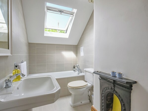 A bathroom with a skylight, a bathtub, a toilet, and a fireplace.