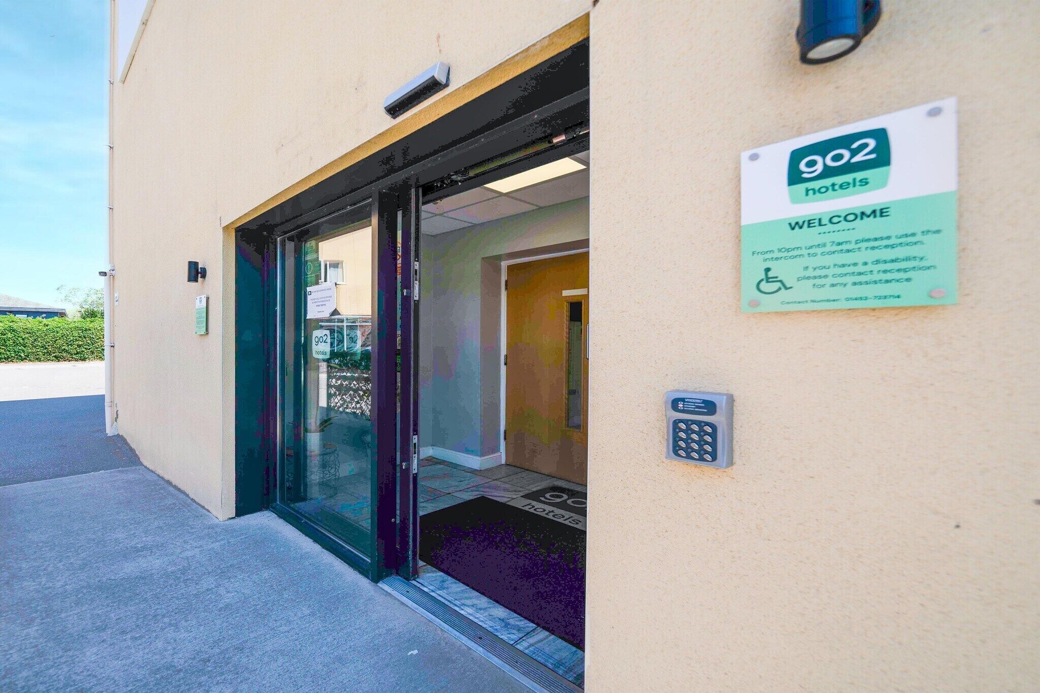 Entrada de hotel con puerta de vidrio, cartel de bienvenida y símbolo de accesibilidad para sillas de ruedas.
