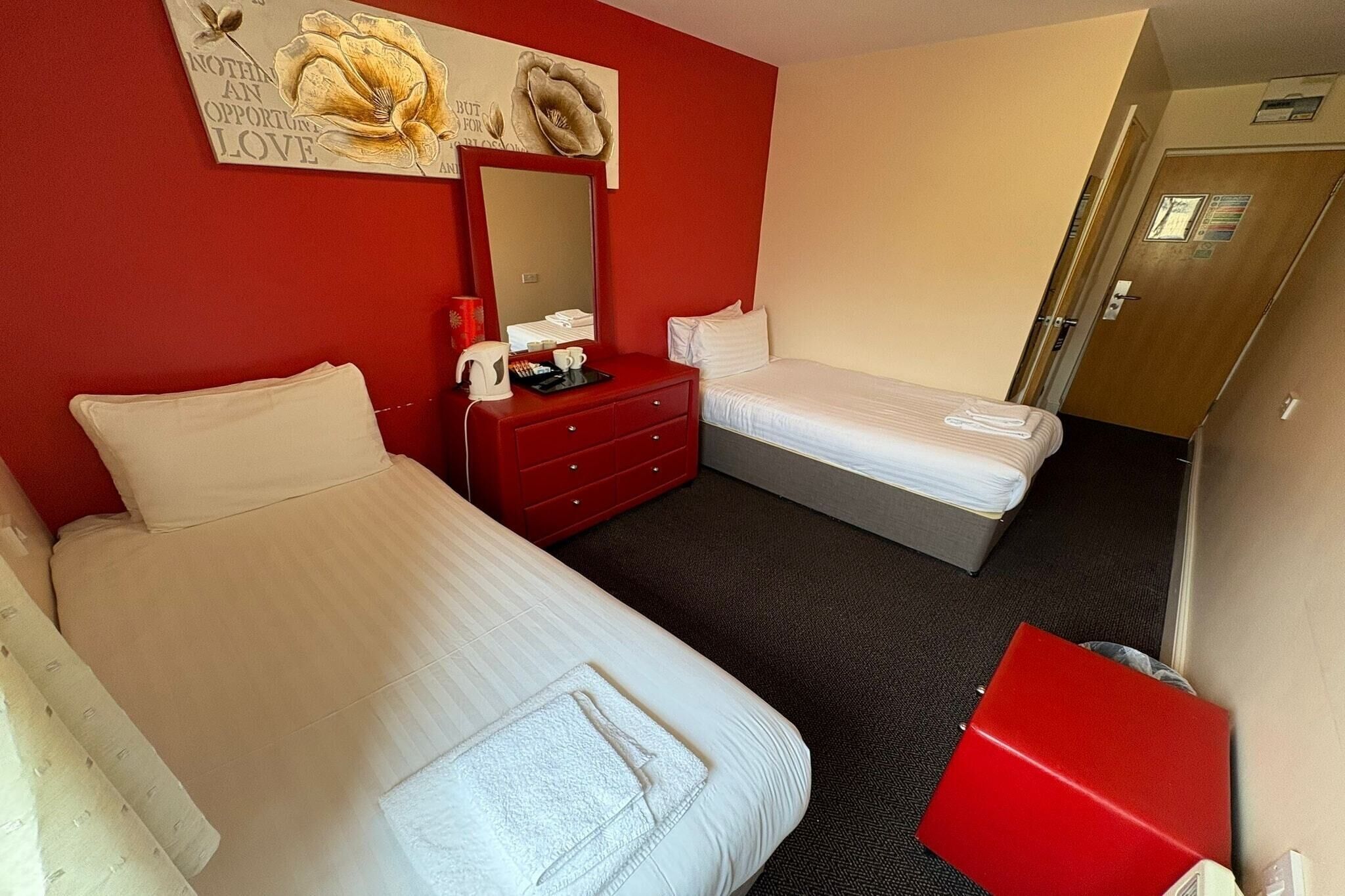 A hotel room with two beds, a red dresser, a mirror, and a red cabinet.