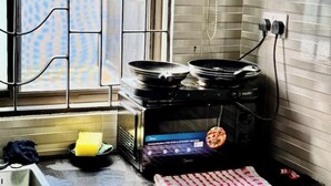 Una cocina con estufa, dos sartenes, una esponja amarilla y un mantel a cuadros rojo y blanco sobre la encimera.
