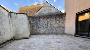 Une terrasse sur le toit, dotée d’un sol en pierre, d’une rambarde en métal et offrant une vue sur un bâtiment dont le toit est en pente.
