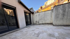 Une cour avec un sol en pierre, un mur en béton et un bâtiment doté de grandes portes vitrées.