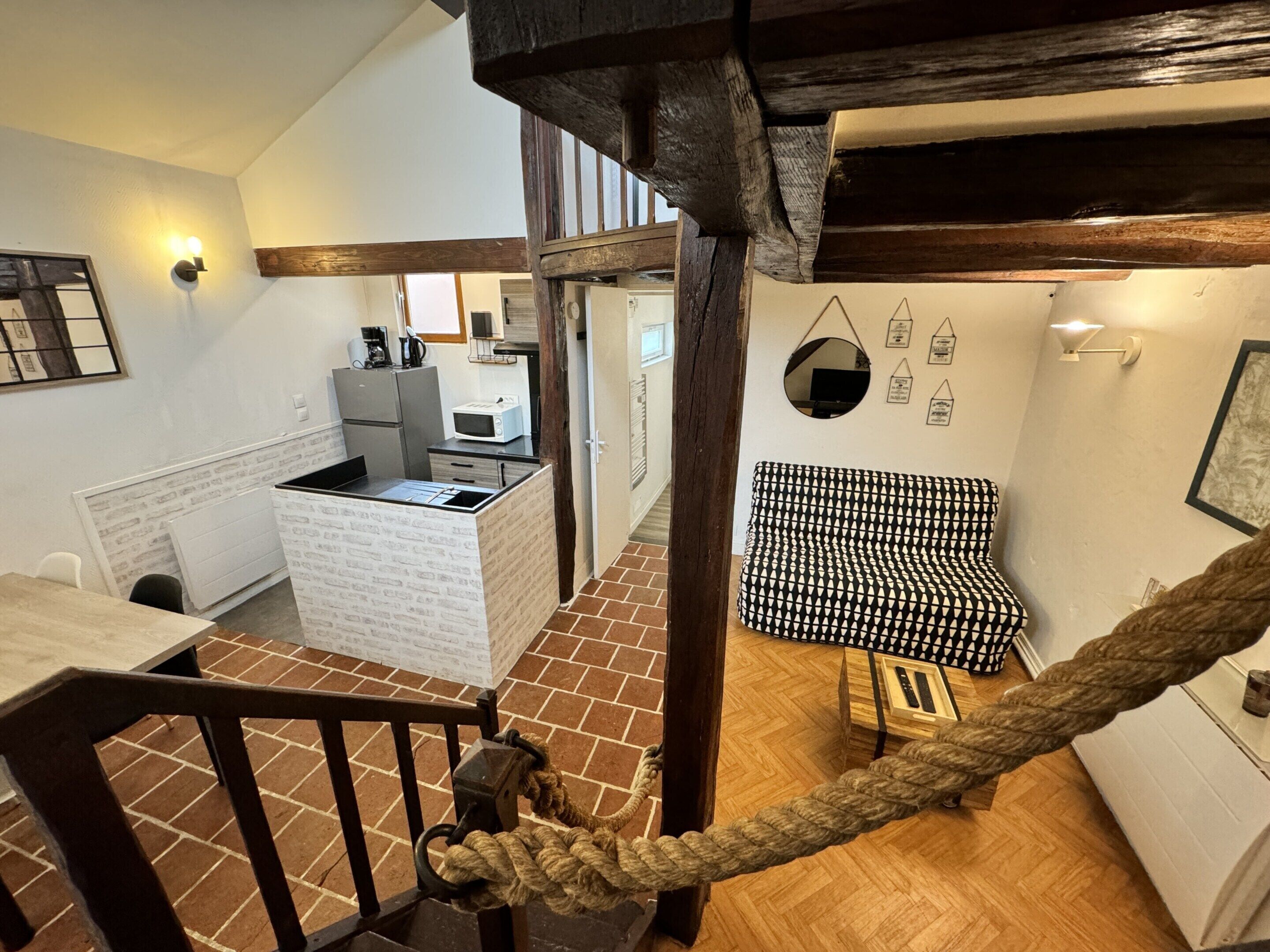 A staircase with a rope barrier, a kitchen area with a microwave, and a patterned sofa.