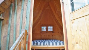 A wooden cabin with a loft-style bedroom featuring a bed with striped bedding and a small window. - Doppelhaushalfte mit Kamin in Hasselfelde (Oberharz am Brocken)