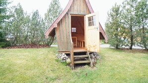 A wooden cabin with a steeply pitched roof and an open door, surrounded by grass and trees. - Doppelhaushalfte mit Kamin in Hasselfelde (Oberharz am Brocken)