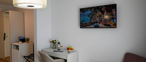 A modern room with a white desk, a chair, a purple sofa, a painting of a coastal scene, and a hanging light fixture.