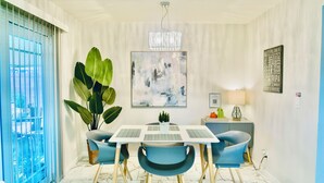 Een eethoek met een tafel, stoelen, een plant in pot, een kunstwerk aan de muur en een lamp.