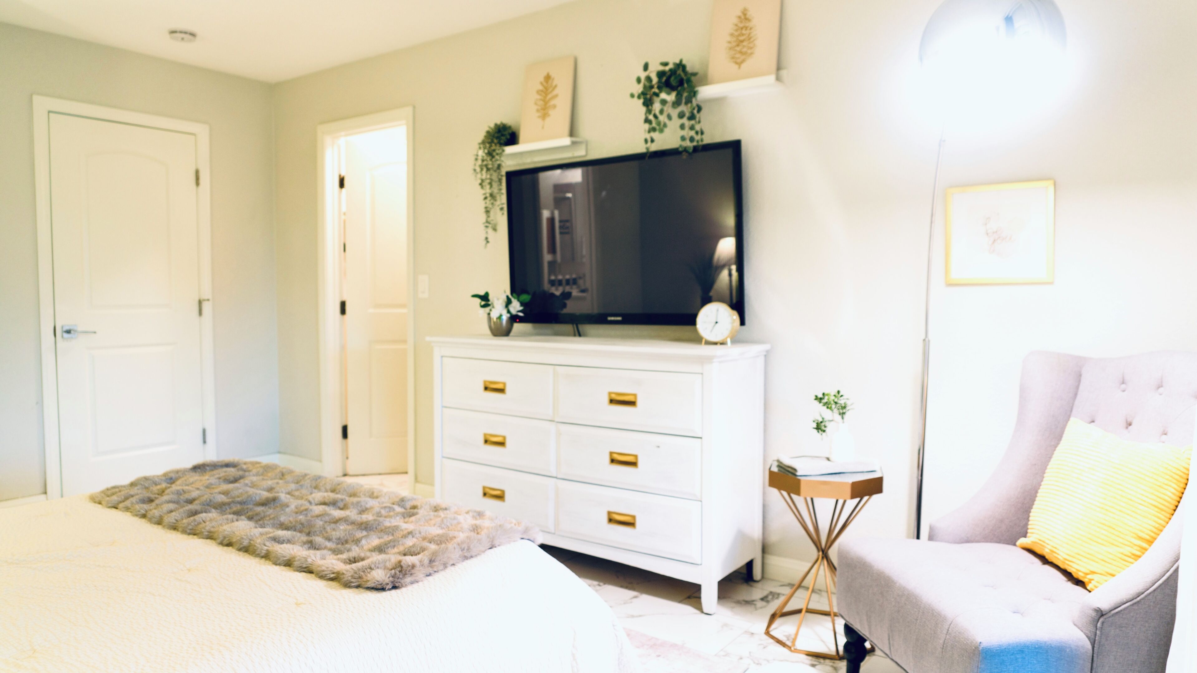Une chambre à coucher avec un lit, un téléviseur posé sur une commode, une chaise et une petite table.