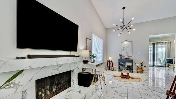 Een moderne woonkamer met een grote flatscreen-tv, een open haard, een eethoek met een tafel en stoelen, en een plafondlamp.