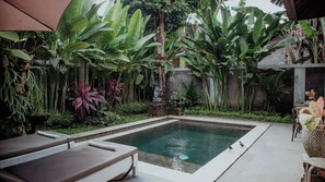 A rectangular pool with a stone border, surrounded by lush greenery and a brick wall. - Genta Villa Ubud (Ubud)