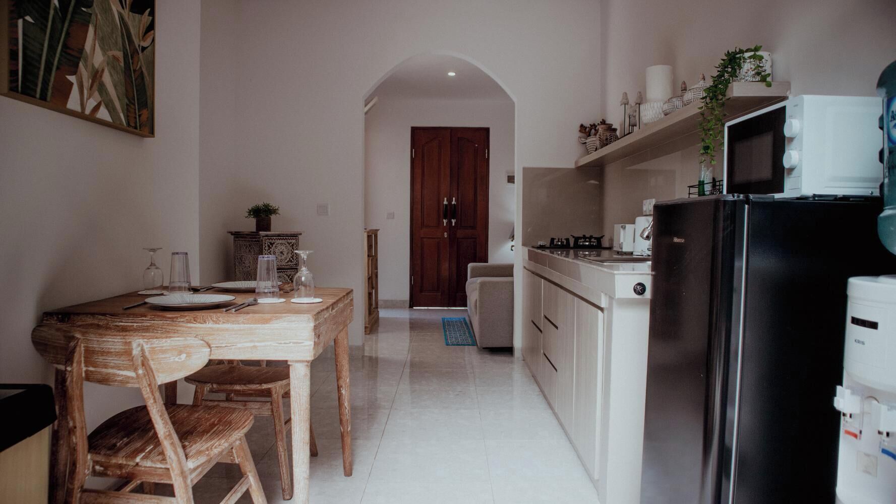 A compact kitchen with a dining area, featuring a wooden table and chairs, a microwave, and a refrigerator.