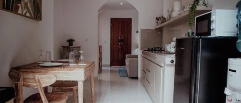 A compact kitchen with a dining area, featuring a wooden table and chairs, a microwave, and a refrigerator.