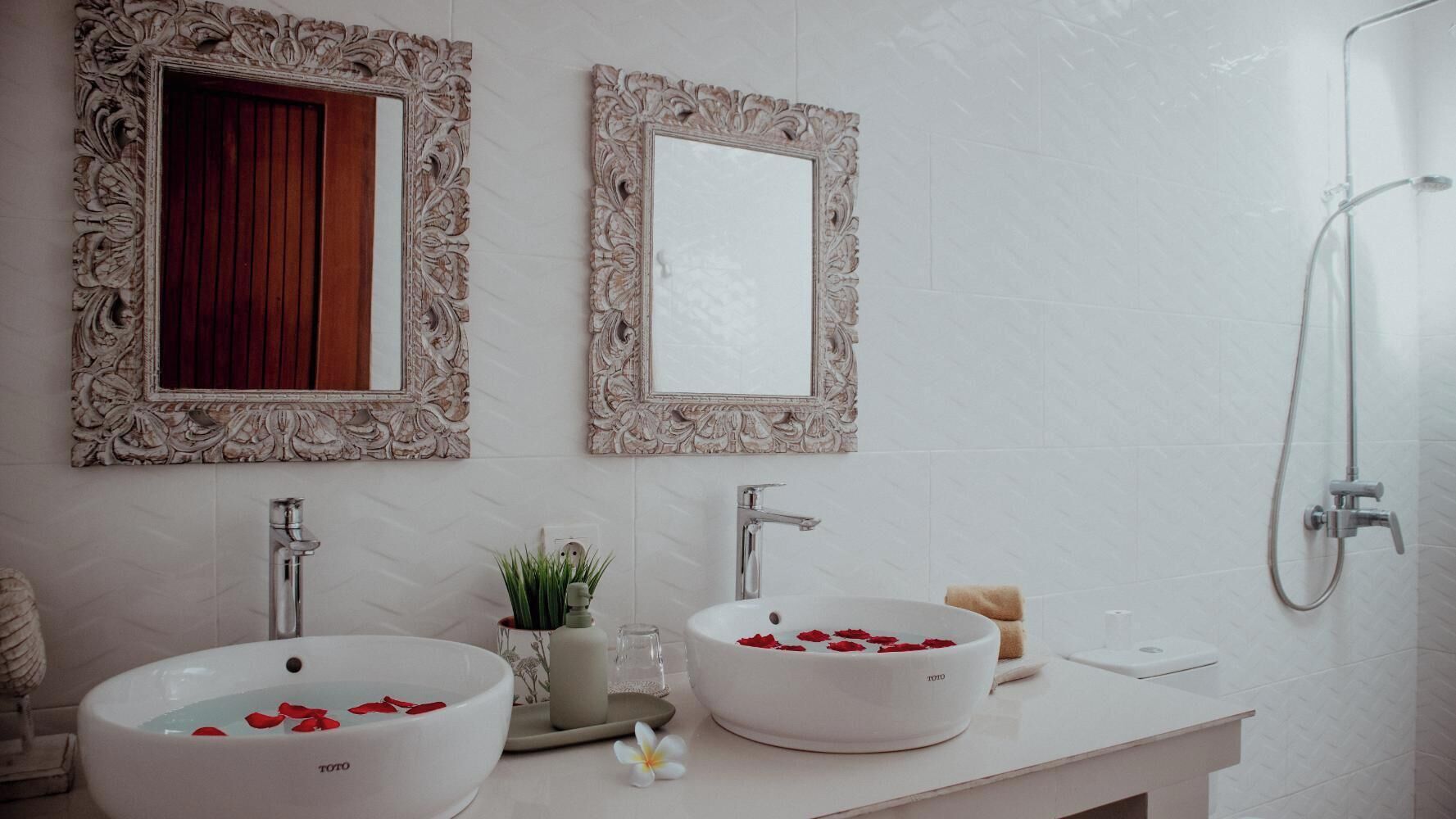 Ein Badezimmer mit zwei weißen Waschbecken, einer Dusche und verzierten Spiegeln.