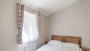 A bedroom with a bed, a nightstand, a radiator, and a window with curtains. - Caravan with one double and two twin. (Longridge, Ribble Valley)