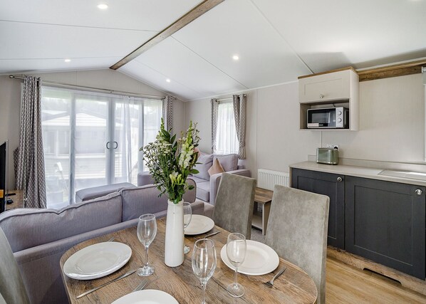 A modern living room with a sofa, dining table set for four, and a kitchen area with a microwave.