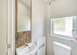 Ein Badezimmer mit einem weißen Waschbecken, einem Spiegel, einem Fenster und einer Toilette.