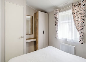 Ein Schlafzimmer mit einem Bett, einem Kleiderschrank, einem Spiegel und einem Fenster mit Vorhängen.