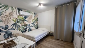 Een kleine, verzorgde kamer met een bed, een gedekte tafel en een muur met een tropisch bladpatroon.