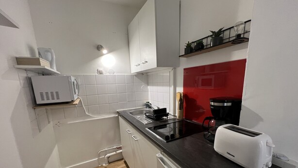 Een kleine keuken met een zwart aanrecht, witte kastjes, een broodrooster en een koffiezetapparaat.