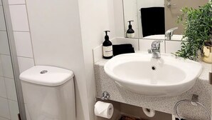 Une salle de bain moderne avec des toilettes blanches, un lavabo surmonté d’un miroir et un tableau encadré représentant un renard accroché au mur.