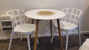 Une petite table ronde blanche, surmontée d’un set de table en fibres tressées, et entourée de deux chaises en plastique blanc aux pieds en bois.