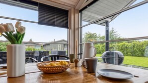 A dining area with a wooden table, a vase with tulips, a basket of bread, and a grill outside the window.