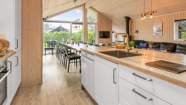 A modern kitchen with a wooden ceiling, large windows, and a dining area with chairs and a table.