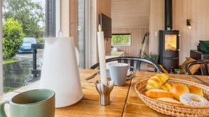 A cozy room with a wooden interior, a large window, a table with breakfast items, and a wood-burning stove.