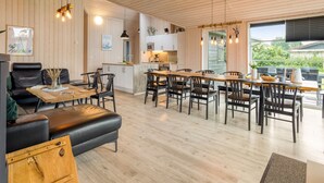 A spacious living area with a wooden floor, a black leather sofa, a wooden coffee table, and a dining area with a long table and chairs.